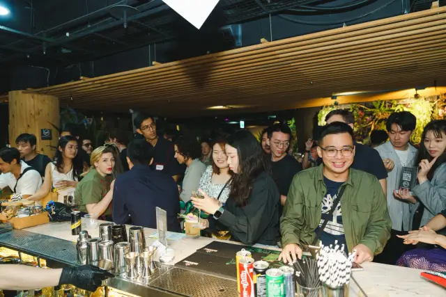 吧台旁的晚間交流，參加者靠著吧台笑著看向鏡頭