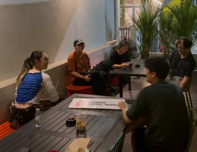 清邁遊牧創作之旅，幾個人圍坐在戶外木桌旁，桌上有 Taiwan Digital Nomad 的牌子