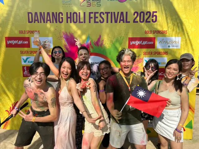 越南活動現場，一群人在「DANANG HOLI FESTIVAL 2025」背板前擺姿勢，其中一人舉著台灣國旗